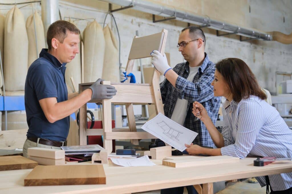 Group of working designers discussing production of new model of wooden modern chair, background carpentry workshop
