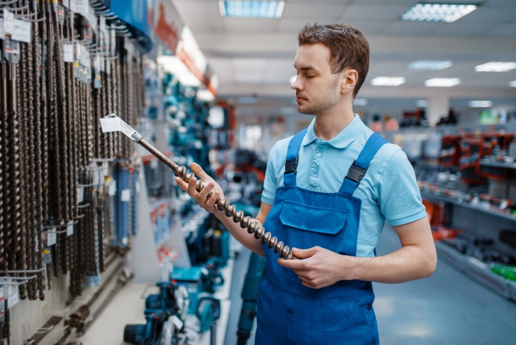 Male employee in uniform choosing concrete drill in tool store. Choice of professional equipment in hardware shop, instrument supermarket