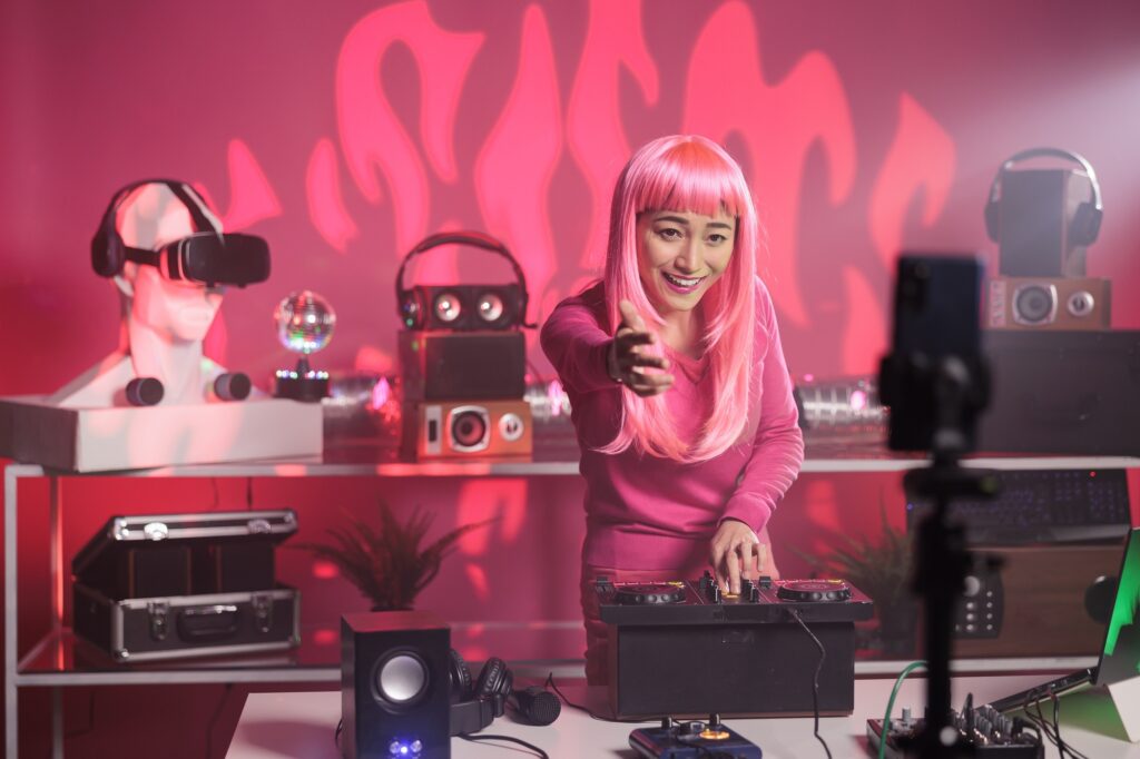Asian dj artist recording music session with mobile phone camera while playing song at mixer console, standing in audio studio over pink background. Smiling woman checking sound celebrating night life