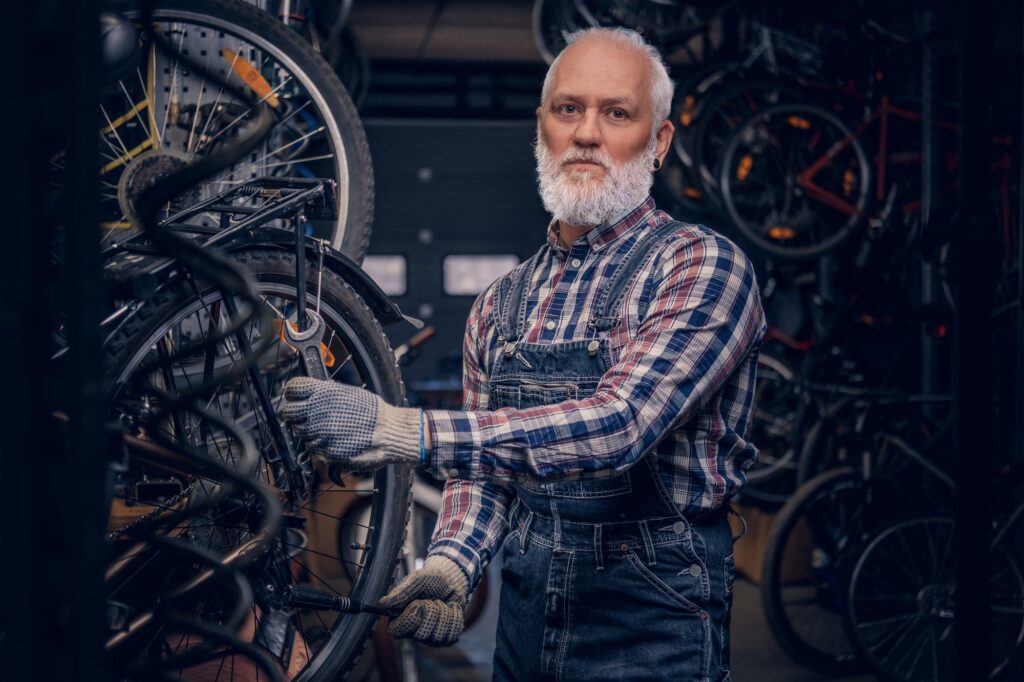 Photo of professional elderly craftsman working repairing bicycles in workshop.