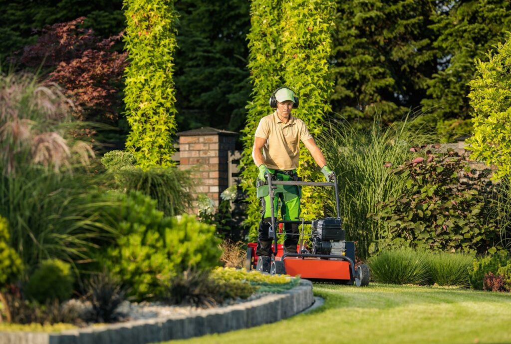 Large and Beautiful Landscape Garden in the Backyard of Residential House. Professional Landscaper in Protective Headphones Taking Care of Design Appearance by Mowing the Lawn.